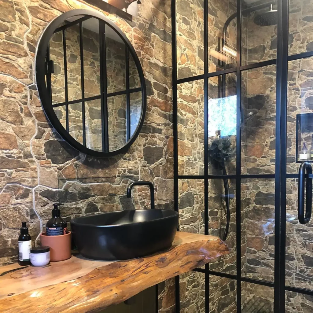 Top 10 Innovative Bath Storage Solutions for Every Bathroom 4 Rustic shower design with stone wall tiles, black-framed glass panels, and a round mirror, created by Bathrooms Renovations Hamilton.
